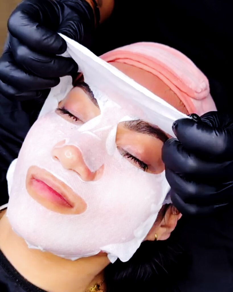 Facial sheet mask application at pygmentarte, professional skincare treatment in Amsterdam, with black gloves.